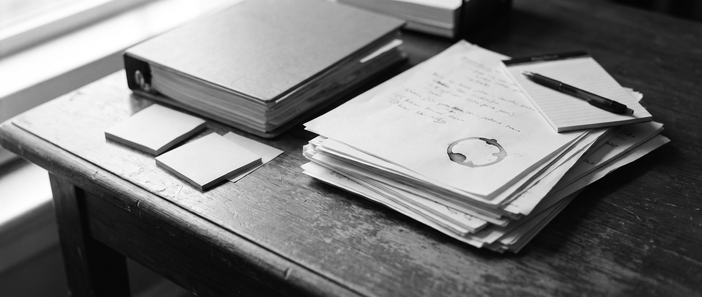 Een bureau vol uitgeprinte spreadsheets, een ordner en memoblaadjes met aantekeningen